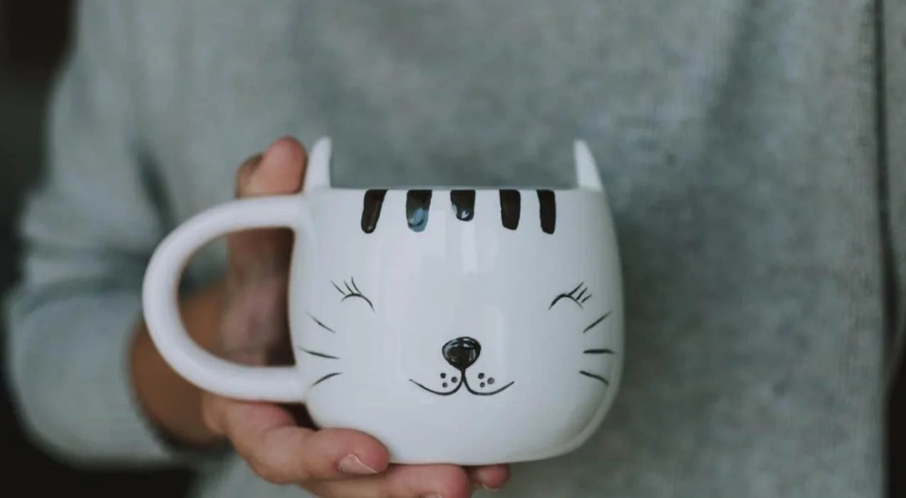 close-up of a hand holding a black and white cat mug