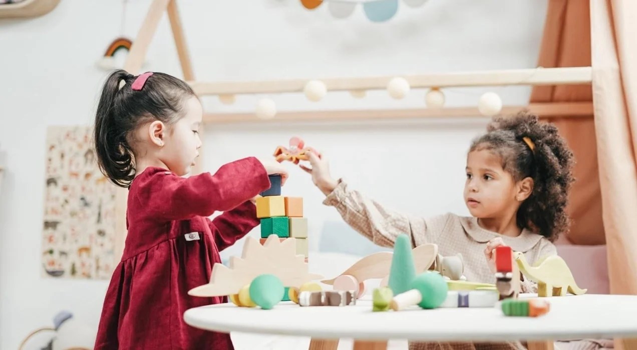 two children playing with wooden toys at a small table